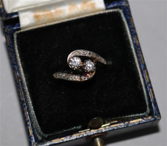 A gold and two stone diamond crossover ring with diamond set shoulders, size M.